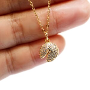 May include: A gold chain necklace with a charm shaped like a fortune cookie. The charm is covered in small, clear rhinestones.