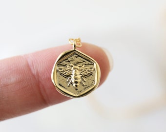 Peut inclure: Collier en or avec un pendentif hexagonal représentant une abeille détaillée.