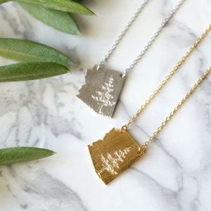 May include: Two necklaces with a tree pendant. One necklace is silver and the other is gold.