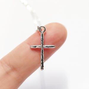May include: A silver cross pendant necklace with a textured finish. The cross is on a silver chain.