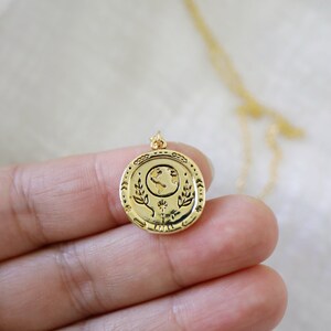 Op de afbeelding: Gouden ketting met een ronde hanger met een gegraveerd beeld van de aarde, omringd door bladeren en een bloem.