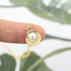 Op de afbeelding: Een goudkleurige ketting met een schelphanger en een witte parel. De schelphanger heeft een gestructureerd, geribbeld ontwerp. De ketting zit aan een gouden ketting.