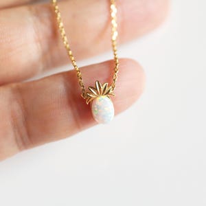 May include: A gold chain necklace with a small white opal pineapple pendant.