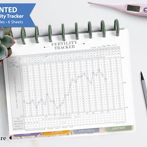 Puede incluir: Un rastreador de fertilidad impreso con 12 ciclos y 6 hojas. El rastreador está abierto en una página con un gráfico y datos de febrero y marzo. Un termómetro digital muestra 37 grados Celsius. Un bolígrafo gris descansa al lado.