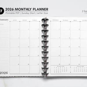 May include: Open 2026 monthly planner with a Sunday start, printable PDF, and letter size. The planner is open to January, with a grid layout for each day. The planner has a black and white checkered design on the side and gold accents.