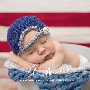 May include: A sleeping baby wearing a blue and gray crocheted baseball cap with a white baseball button. The baby is lying in a white bucket with a blue and gray crocheted blanket.