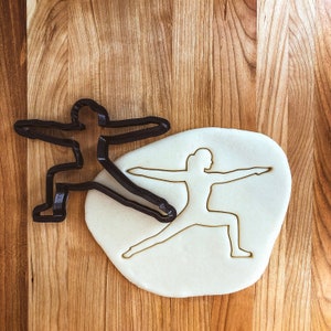 May include: A black plastic cookie cutter in the shape of a person in a yoga pose, with a white dough cutout of the same pose.