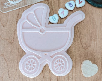 May include: A pink plastic baby carriage cookie cutter with the word "BABY" spelled out in colourful heart-shaped beads.
