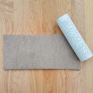 Peut inclure: Un rouleau à pâtisserie gris avec un motif floral et une feuille texturée grise assortie. Le rouleau à pâtisserie et la feuille sont sur une surface en bois.