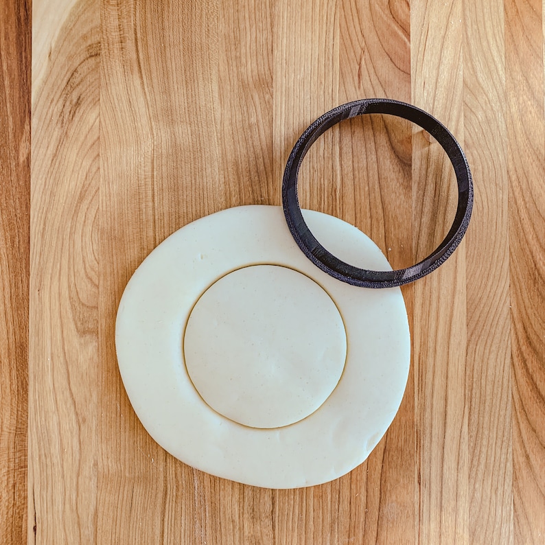 Pu&ograve; includere: Un cerchio di pasta di zucchero bianca con un cerchio pi&ugrave; piccolo tagliato al centro. Un anello di plastica nero &egrave; posto sopra la pasta di zucchero.