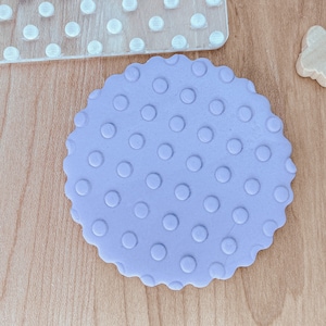 May include: A purple fondant circle with a polka dot pattern. The fondant is embossed with a circular pattern.