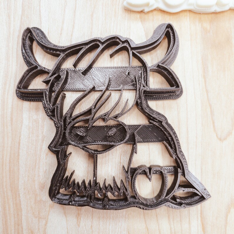 Puede incluir: Cortador de galletas de pl&aacute;stico negro con forma de vaca de las tierras altas con una melena esponjosa y una nariz en forma de coraz&oacute;n.