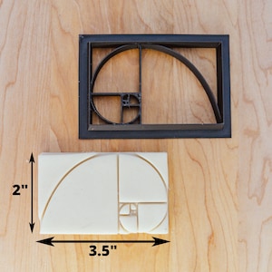 May include: A white plastic mould of the Fibonacci spiral, measuring 3.5 inches wide and 2 inches tall. The mould is used to create a decorative design in soap, fondant, or other materials.