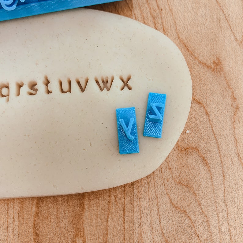 May include: Blue plastic alphabet stamps with the letters qrstuvwxyz and v and z on a white surface.