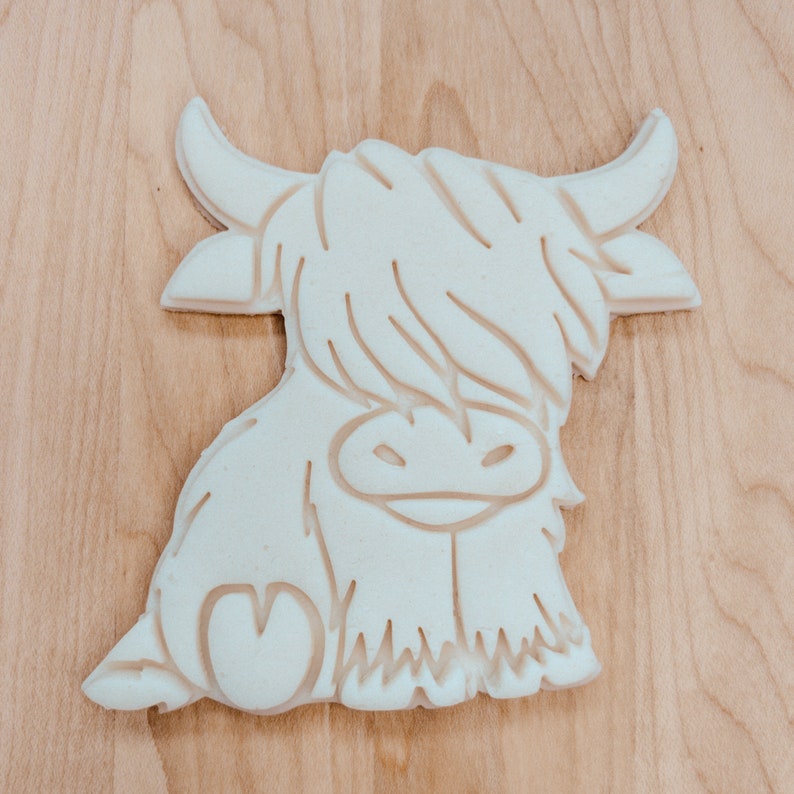 Puede incluir: Cortador de galletas de pl&aacute;stico blanco con forma de vaca de las tierras altas con un coraz&oacute;n en un lado.