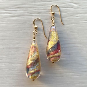May include: A pair of gold teardrop earrings with a clear glass design featuring swirls of gold, pink, and gray.