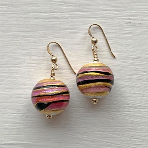 May include: Gold earrings with pink, black, and gold striped glass spheres.