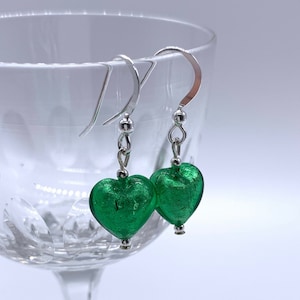 May include: A pair of silver dangle earrings with green heart-shaped glass beads. The glass beads have a metallic finish.