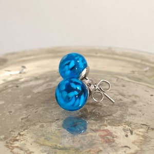 May include: A pair of blue glass stud earrings with white flecks inside. The earrings have silver posts and backs.