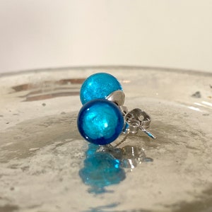 May include: A pair of blue glass stud earrings with silver posts. The earrings are round and have a sparkly finish.