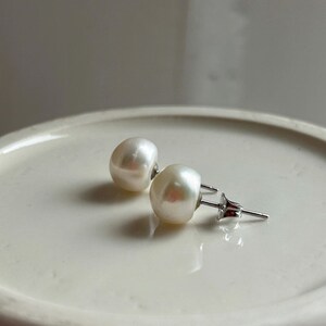 May include: A pair of white pearl stud earrings with silver posts.