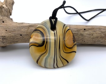 May include: A round, cream-colored glass pendant with brown and black swirling patterns. The pendant is attached to a black cord.
