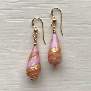 May include: A pair of gold dangle earrings with pink and gold glass teardrop shaped beads. The beads have a swirl pattern and gold flecks.