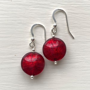 May include: A pair of silver dangle earrings with red glass round beads. The beads have a textured, iridescent finish.