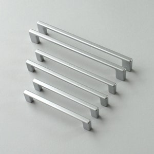 Könnte beinhalten: Fünf silberne Schrankgriffe in verschiedenen Längen, in einer Reihe vom längsten zum kürzesten angeordnet.