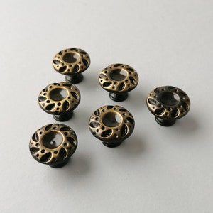 May include: Six antique gold cabinet knobs with a black base and a decorative floral design.