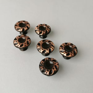 May include: Six copper-toned cabinet knobs with a black finish and a decorative floral design.