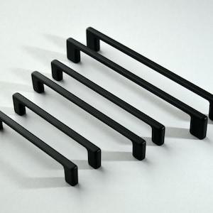 Peut inclure: Six poignées de meuble en métal noir de différentes longueurs. Les poignées ont une forme rectangulaire aux bords arrondis.