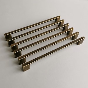 Peut inclure: Six poignées de porte en laiton antique de forme rectangulaire et légèrement incurvée. Les poignées sont disposées en quinconce.