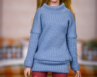 May include: A doll wearing a blue waffle knit sweater and red patterned leggings.