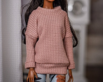 May include: A doll with dark brown hair wearing a pink knitted sweater and blue and white patterned pants.