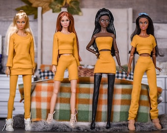 May include: Four fashion dolls wearing matching mustard yellow outfits. The dolls have different hairstyles and skin tones. The dolls are standing in front of a plaid blanket.