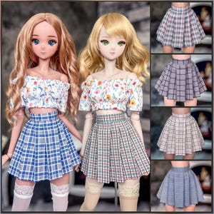 Op de afbeelding: Twee poppen dragen off-the-shoulder bloemen tops en geplooide rokken. De rokken zijn in blauw en wit, en rood en groen geruite patronen. De afbeelding toont ook een selectie van geruite rokken in verschillende kleuren. Tekst links leest "Geplooide rok" en rechts "1/3 scale Classic".