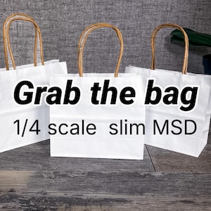 May include: Three white paper gift bags with brown twisted paper handles. The bags have the text "Grab the bag" and "1/4 scale slim MSD" printed on them. The bags are on a wooden surface.