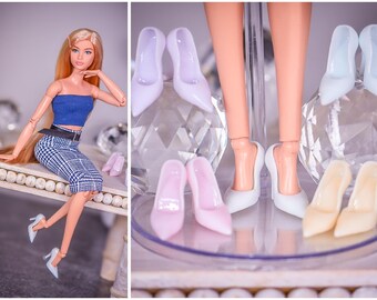 Puede incluir: Una muñeca de moda con cabello rubio largo, que lleva un top corto azul, una falda a cuadros en blanco y negro y tacones azul claro. Se exhiben varios pares de tacones altos en miniatura de varios colores.