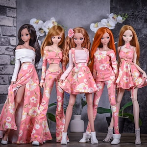 May include: Five dolls wearing pink floral outfits. The dolls have long hair and are wearing white shoes. The dolls are standing in front of a brick wall and a gray background.