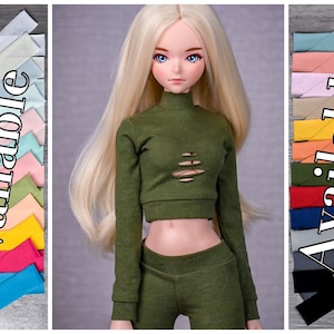 Op de afbeelding: Een groen crop top met lange mouwen en distressed details. Het topje wordt gecombineerd met een bijpassende groene broek. De afbeelding toont een verscheidenheid aan stofkleuren die beschikbaar zijn voor het topje en de broek.