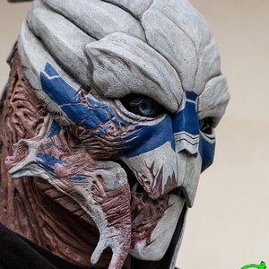 Peut inclure: Un masque d'alien détaillé, peint à la main, gris et bleu avec une surface texturée et sculptée. Le masque a une grande bouche ouverte et des yeux bleus.