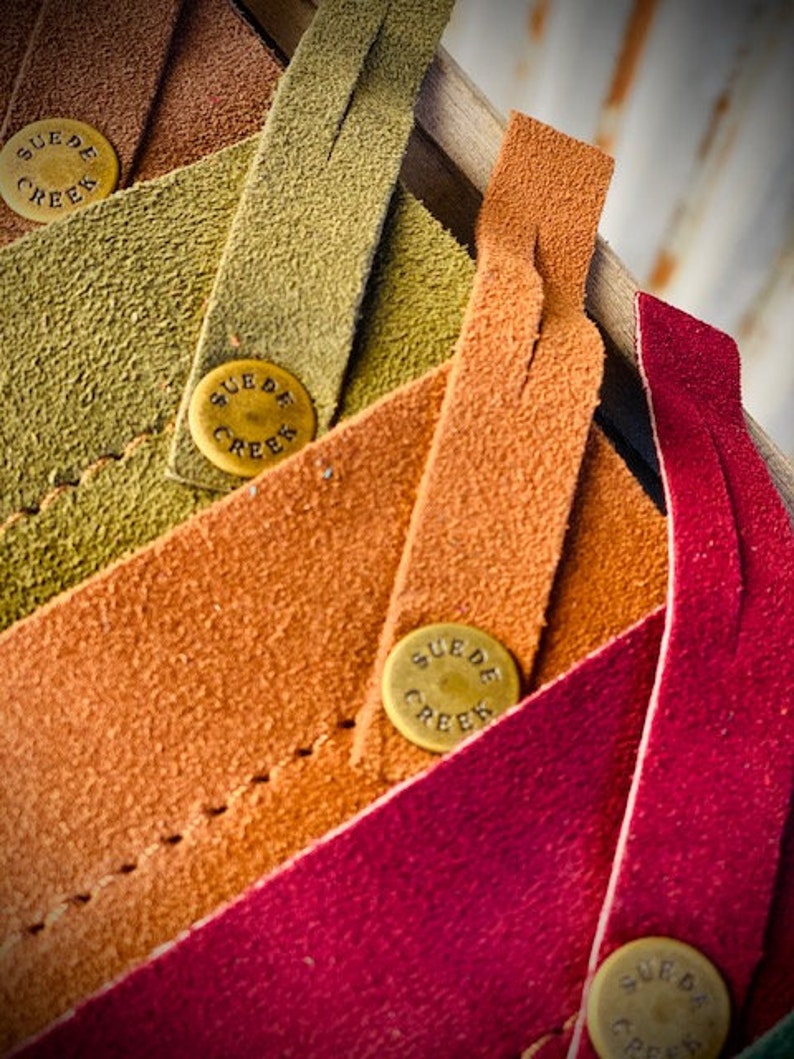 May include: Five strips of leather in different colors, each with a brass tag that reads "SUEDE CREEK". The colors are brown, green, orange, red, and burgundy.