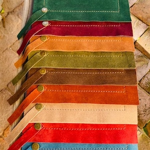 May include: A set of nine placemats in various colors, including green, brown, orange, beige, red, and blue. Each placemat has a stitched border and a small button detail.