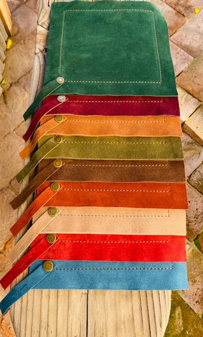 May include: A set of nine placemats in various colors, including green, brown, orange, beige, red, and blue. Each placemat has a stitched border and a small button detail.