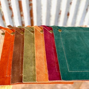 May include: Ten leather coasters in various colors, including blue, red, beige, orange, brown, green, and burgundy. The coasters are square and have a stitched border.