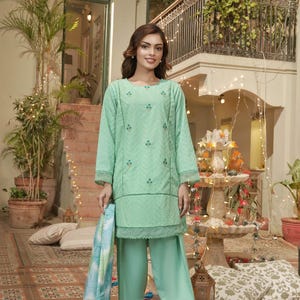 May include: A mint green two-piece outfit with a long-sleeved tunic and wide-leg pants. The tunic features embroidered floral details and a scalloped hem. A matching patterned scarf is held in the hand. The outfit is worn with silver sandals.