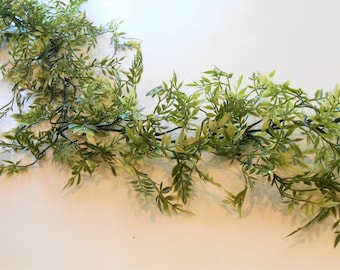 May include: A long, artificial garland featuring small, light green leaves with a touch of yellow. The leaves are clustered along thin, dark brown stems, creating a natural, cascading effect. Ideal for home decor and crafting projects.
