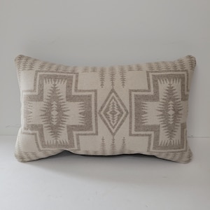 May include: Rectangular decorative pillow with a geometric pattern in shades of beige and gray. The design features cross-like shapes and diamond patterns, creating a Southwestern or Native American aesthetic. The pillow is made of a soft, textured fabric.