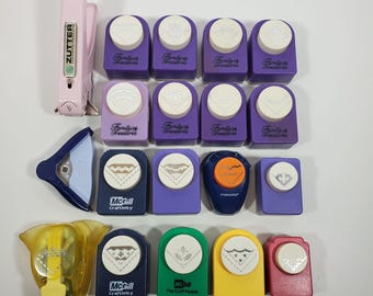May include: A collection of various paper corner punches in assorted colors including purple, blue, green, yellow, red, and light pink. The set includes branded tools from Zutter, Family Treasures, McGill, and Fiskars, each featuring a unique design.